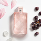 Pink perfume bottle with pink petals and grapes on a white background