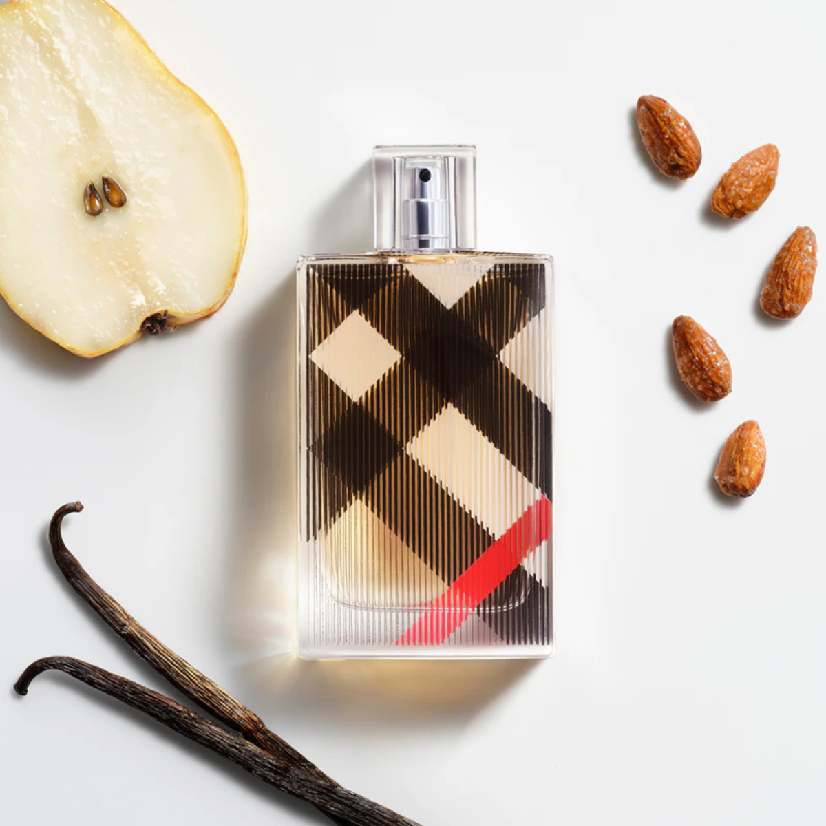 Perfume bottle with checkered design surrounded by vanilla beans, almonds, and a pear slice on a light background