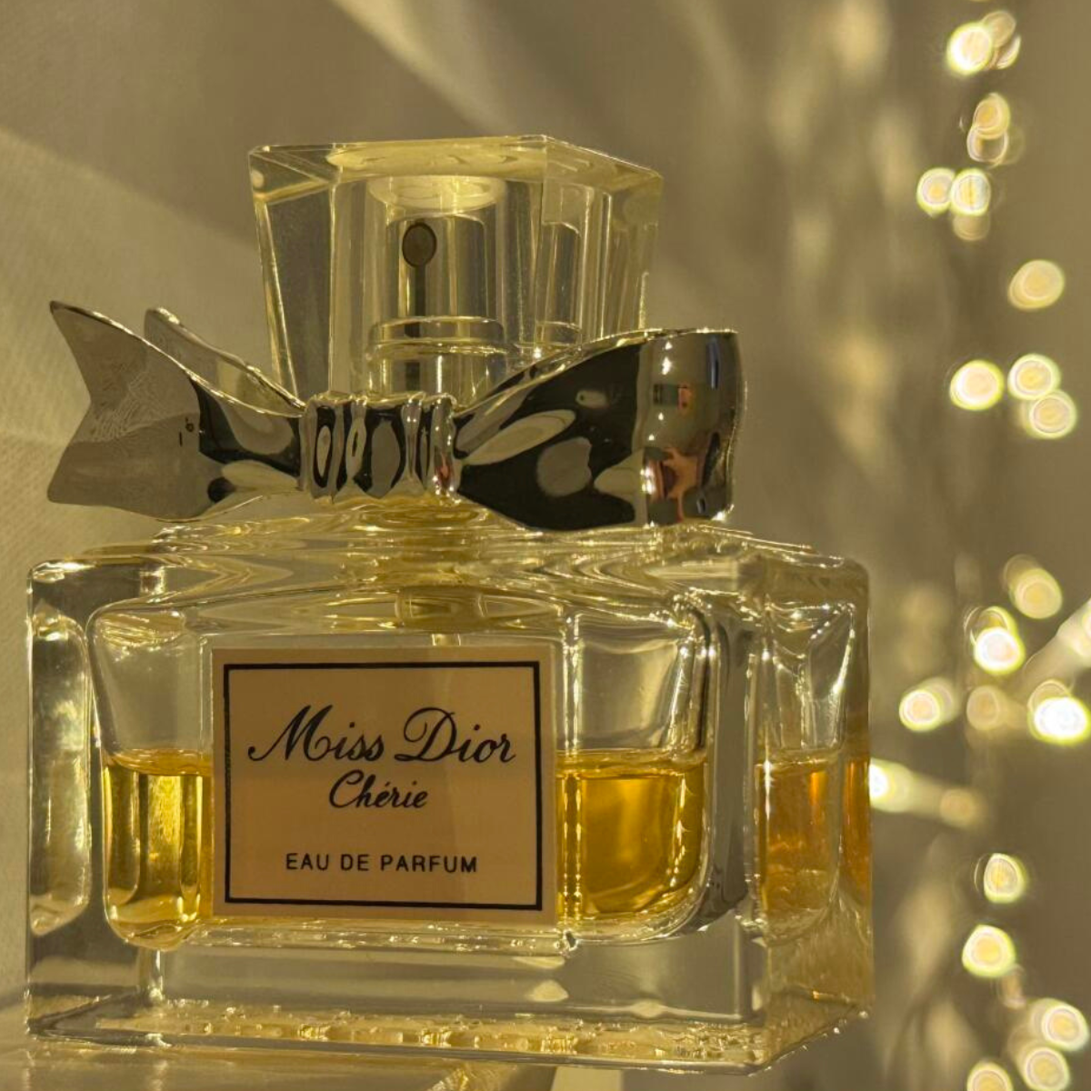 Miss Dior Chérie perfume bottle with a gold cap on a reflective surface.