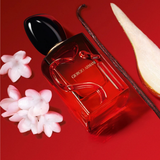 Perfume bottle with flowers and a vanilla bean on a red background