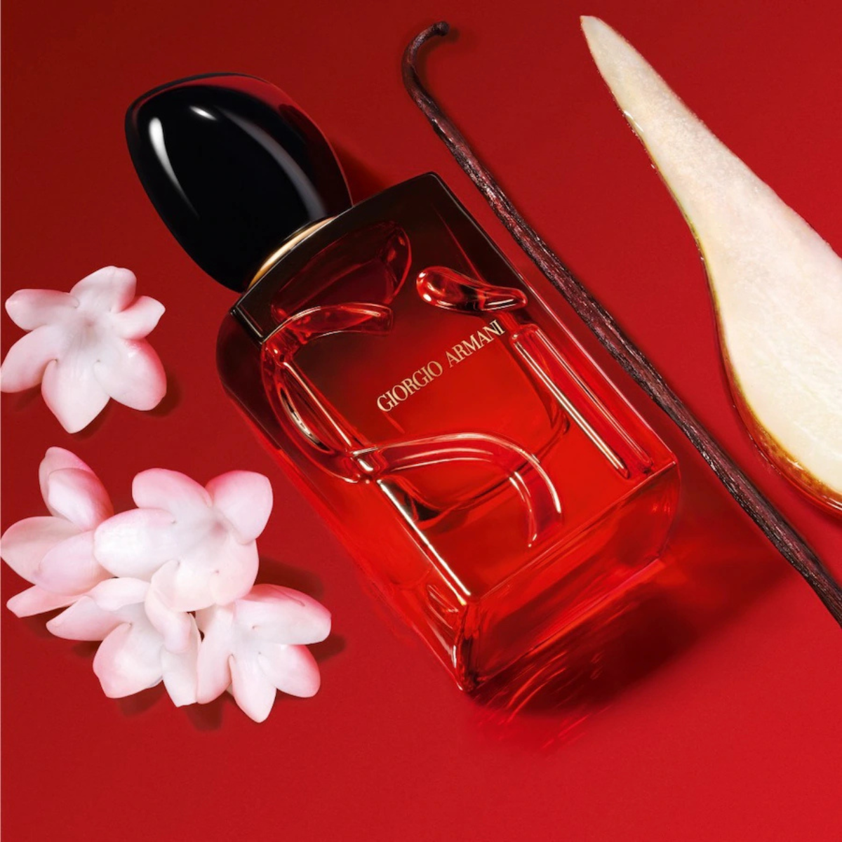 Perfume bottle with flowers and a vanilla bean on a red background