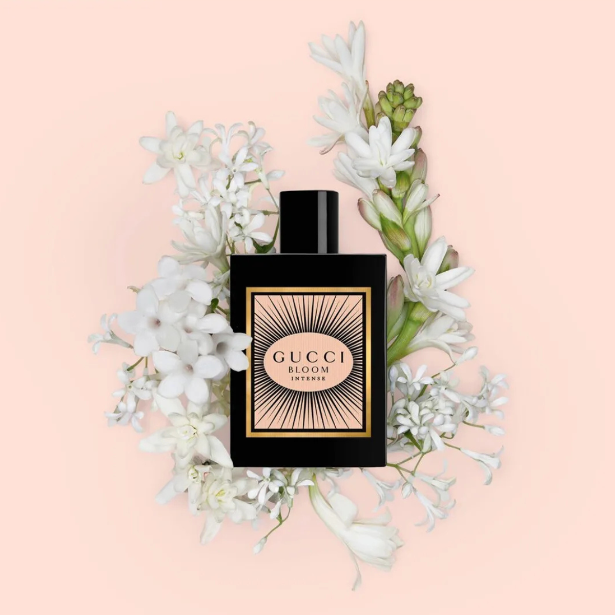 Gucci Bloom Intense perfume bottle surrounded by white flowers on a pink background