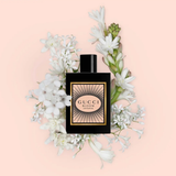 Gucci Bloom Intense perfume bottle surrounded by white flowers on a pink background