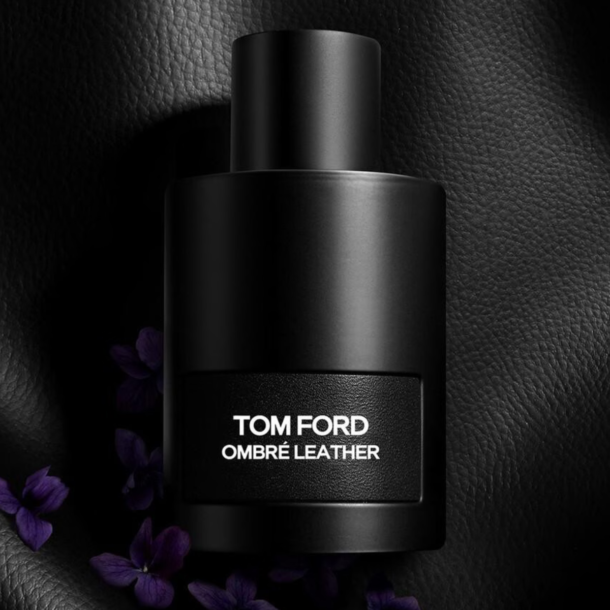Black Tom Ford Ombre Leather perfume bottle on a dark textured background with purple flowers.