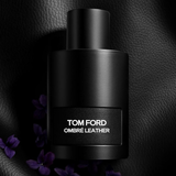 Black Tom Ford Ombre Leather perfume bottle on a dark textured background with purple flowers.