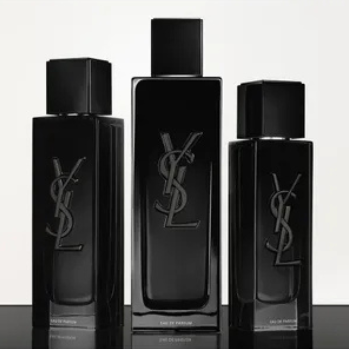 Three black YSL perfume bottles of different sizes on a reflective surface with a white background.